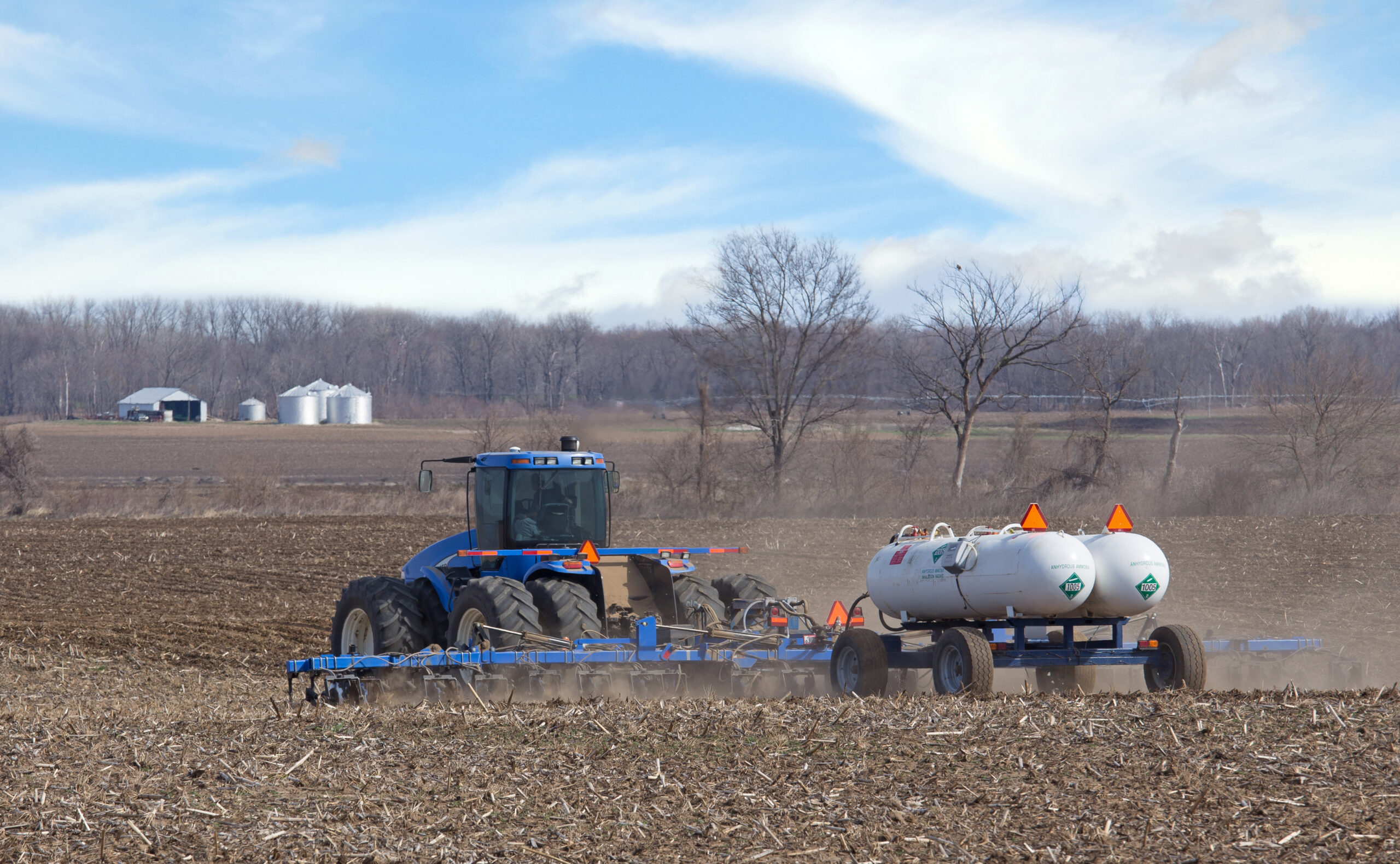 Fertilizing a Farm Field Farm tractor pulling anhydrous ammonia tanks fertilizing farmland